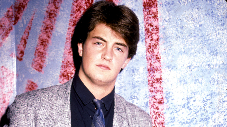 A young Matthew Perry posing in front of a wall