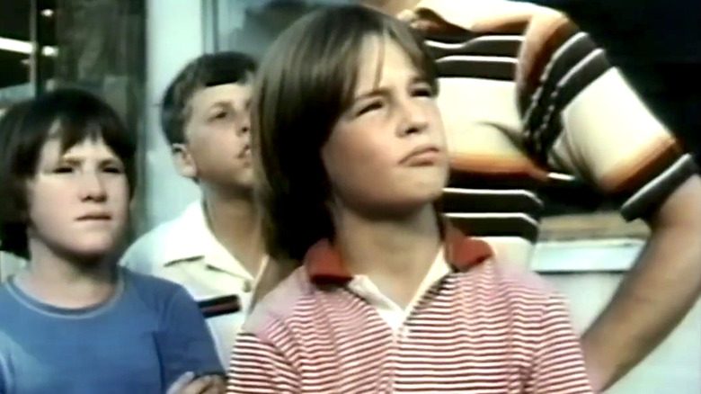 Arthur in a red striped polo shirt standing in front of two other children and a man
