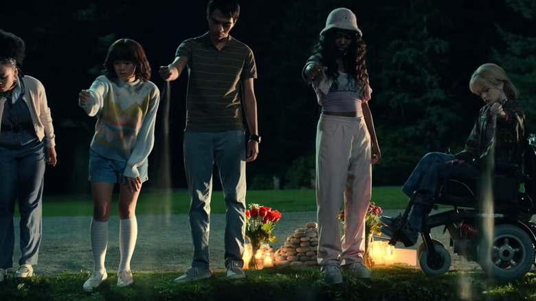 Cheri, Natsuki, Kevin, Ilonka, Anya perform a ritualistic pouring of sand onto the ground before them in The Midnight Club (2022)