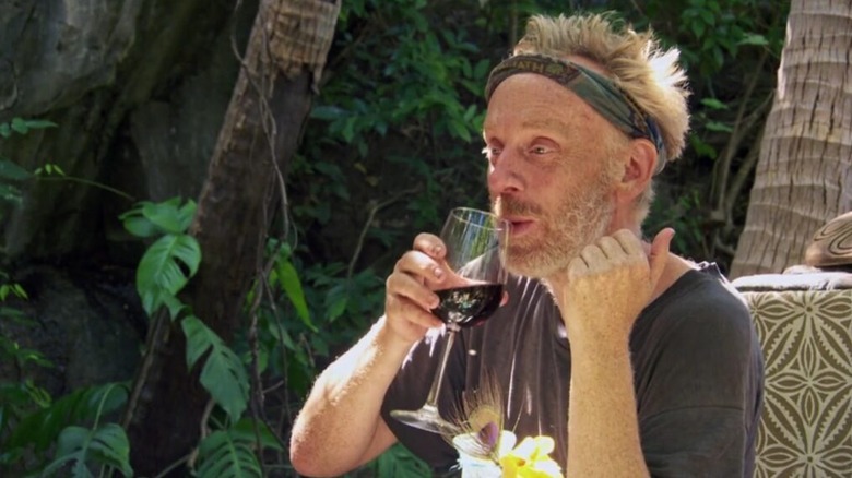 Mike White drinks a glass of wine while wearing a headband across his forehead in the jungle on "Survivor"