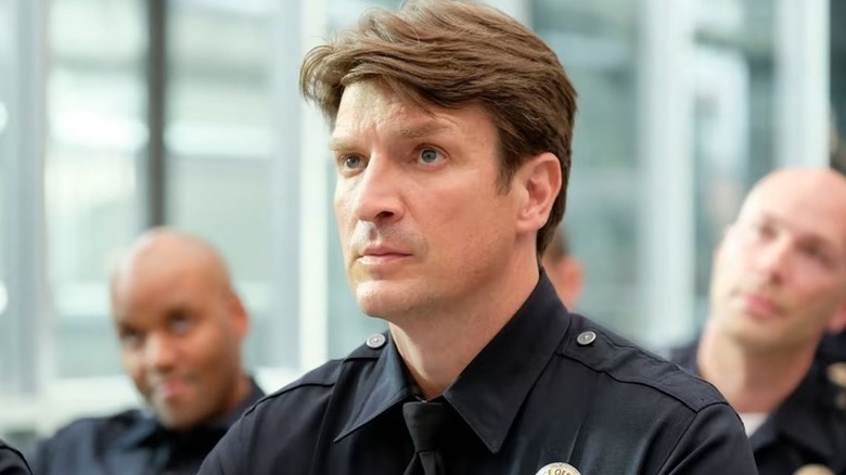 Nathan Fillion as Officer John Nolan sitting down, surrounded by fellow police officers, on "The Rookie"