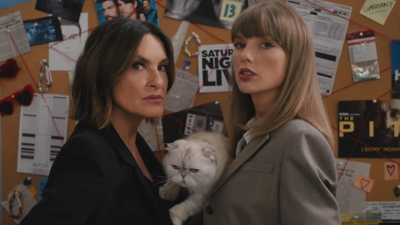 Mariska Hargitay and Taylor Swift stand in front of a board of clues, holding a white cat.