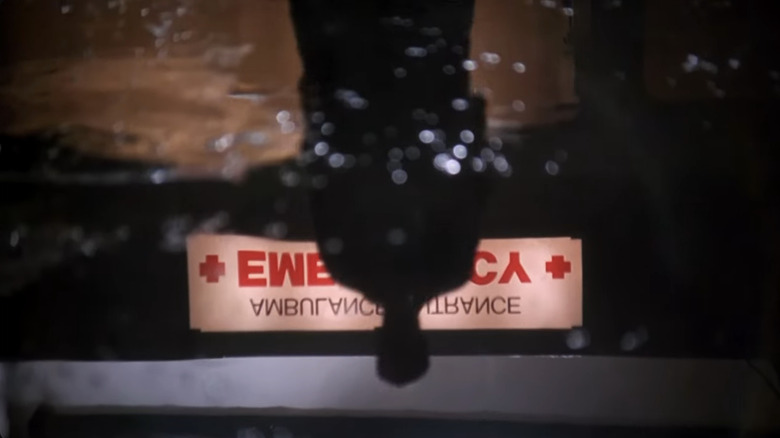 Anthony Edwards as Dr. Mark Greene reflected in shadow upside down in a puddle in the ambulance bay with the upside down emergency sign behind him in ER