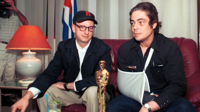 Steven Soderbergh and Benicio Del Toro sitting with an Oscar.