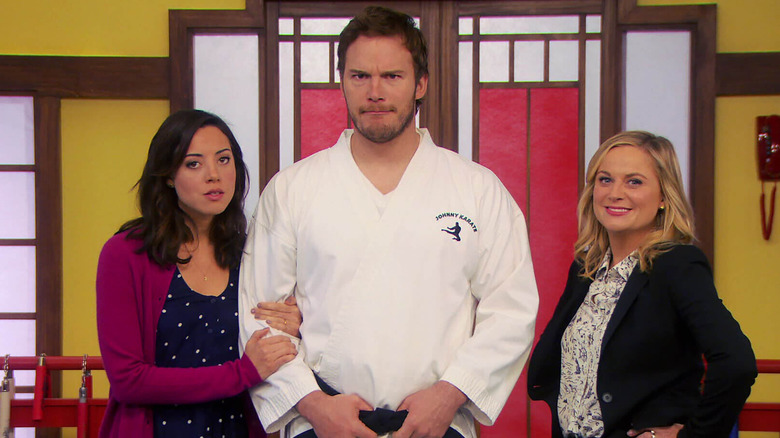 Aubrey Plaza as April Ludgate holding onto Chris Pratt as Andy Dwyer in a gi next to Amy Poehler as Leslie Knope in Parks and Recreation