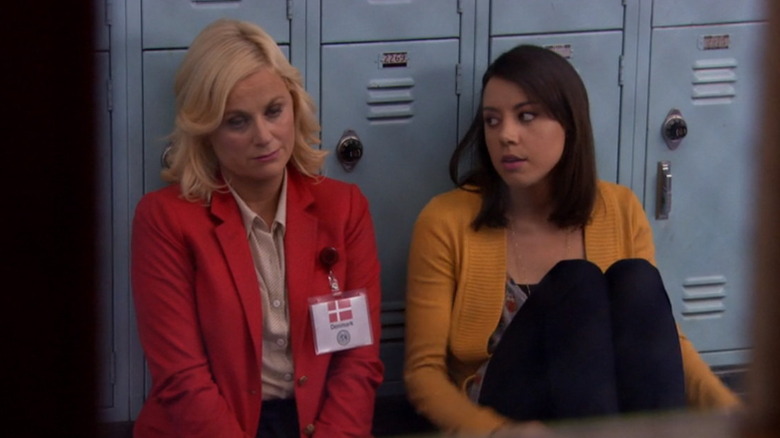 Amy Poehler as Leslie Knope sitting against a locker next to Aubrey Plaza as April Ludgate in Parks and Recreation