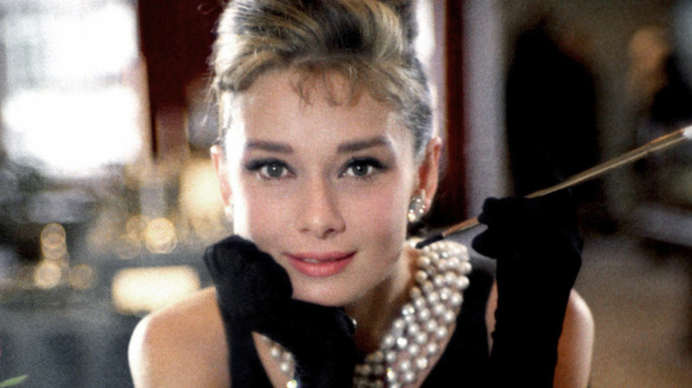 Audrey Hepburn in a high bun, a crown, and long black sleeves, posing with a long cigarette holder in "Breakfast at Tiffany's."