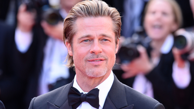 Brad Pitt with swept-back brown hair and a gray goatee wearing a black tuxedo.