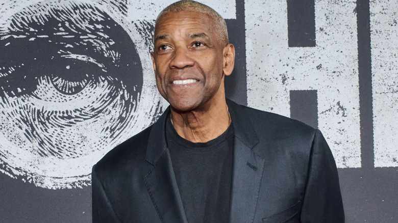 Denzel Washington with short graying hair and wearing a black blazer and t-shirt. He's clean shaven.