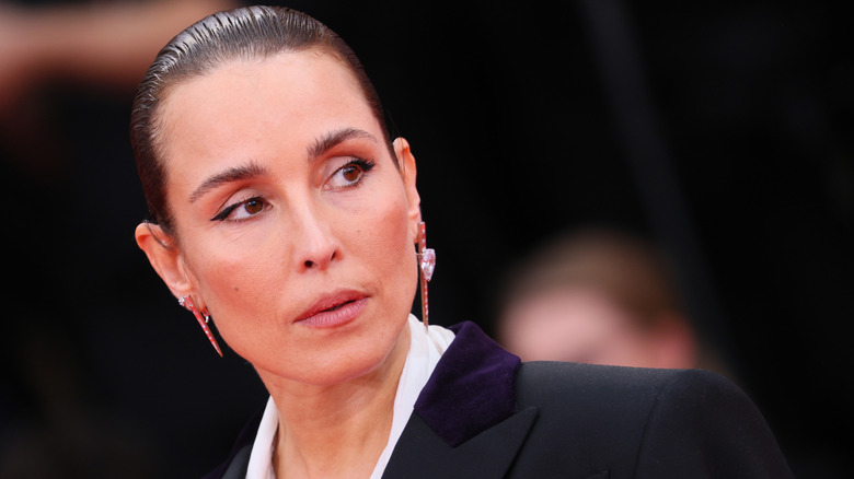 Noomi Rapace with slicked-back hair and looking to the side