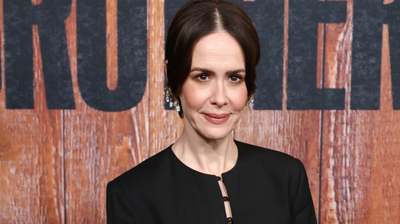Sarah Paulson with her brown hair styled in center parting. She's wearing circular-collard black top with silver earrings.