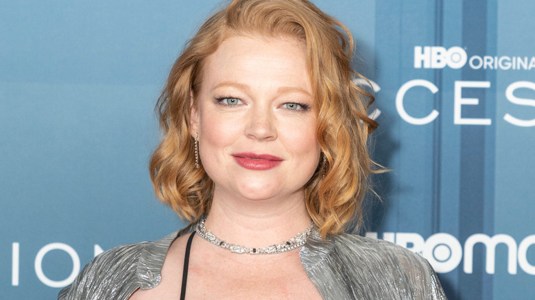 Sarah Snook with her hair in a curly bob. She's wearing a silver jacket with a silver necklace and matching earrings.