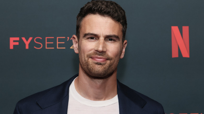 A man with neat brown hair and short stubble is wearing a blue blazer and white t-shirt. He's stood against a black background with red logos for "FYSEE" and Netflix on it.