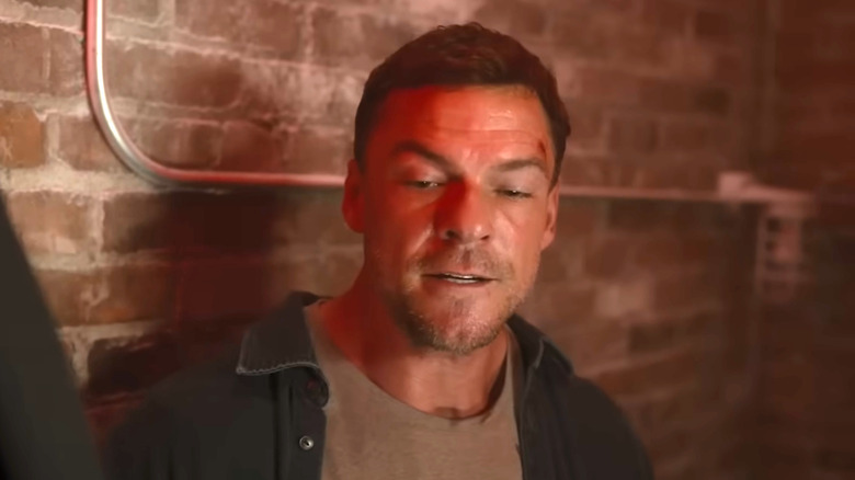 Jack Reacher looking down in front of brick wall