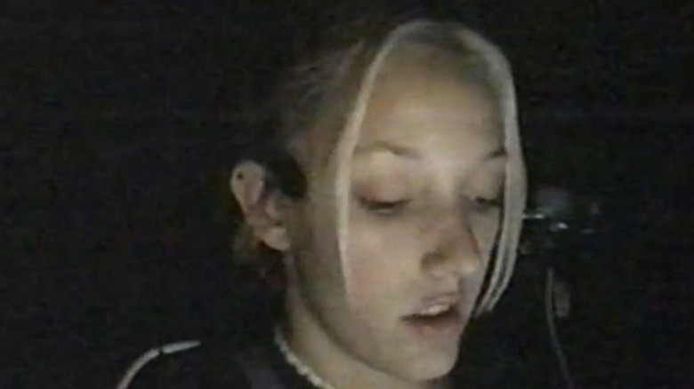 Woman with blonde hair with microphone by ear looking down in dark in Fear