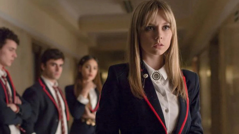 Ester Exposito as Carla standing in a hallway in front of three other students in Elite