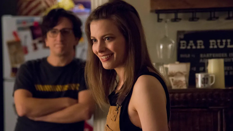 Gillian Jacobs as Mickey smiling while Paul Rust as Gus stands in the background