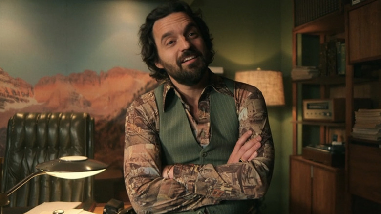 Jake Johnson as Doug sitting in an office smiling in Minx