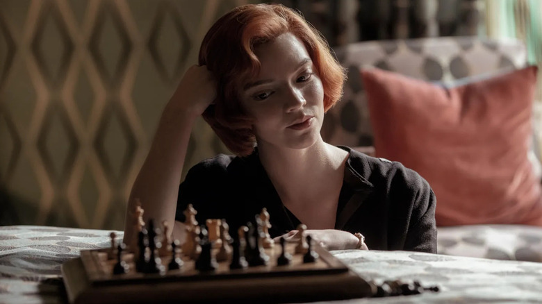 Anya Taylor-Joy as Beth looking at a chess board on a bed in The Queen's Gambit