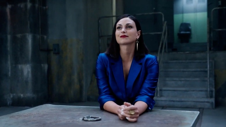 Elena Federova smirking while sitting at a table in a bright blue gown with red lipstick and long earrings
