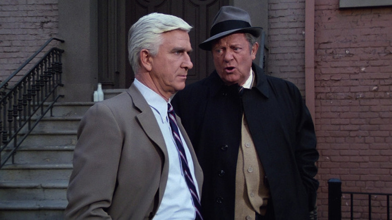 Frank Drebin stares stoically forward while Ed Hocken speaks to him in Police Squad!