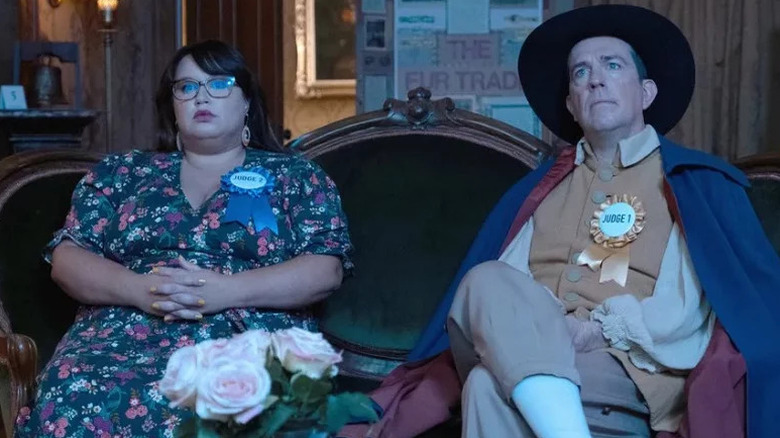 Reagan Wells and Nathan Rutherford sit together on a chaise, with Nathan wearing an outrageous outfit, in Rutherford Falls