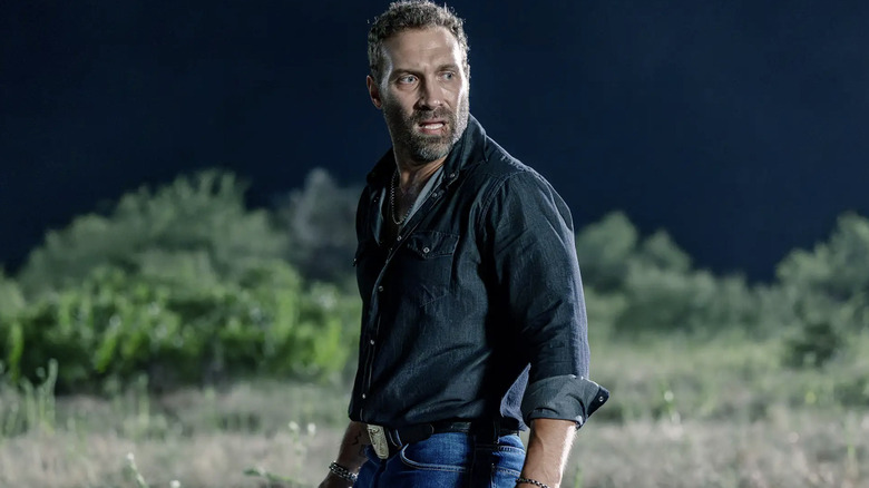 Jai Courtney, Will-Rob Jackson rolünde, kısa siyah saçları ve kısa sakalı var. Koyu mavi bir gömlek ve açık mavi kot pantolon giyiyor.