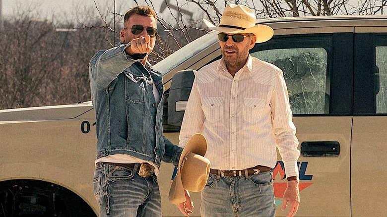 Taylor Sheridan and Billy Bob Thornton standing next to each other in front of a car on the set of Landman