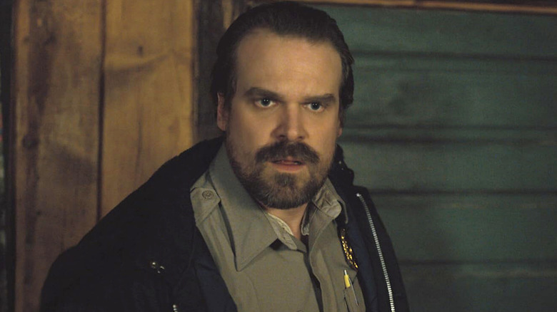 Jim Hopper looking surprised while wearing a black jacket over his tan police uniform