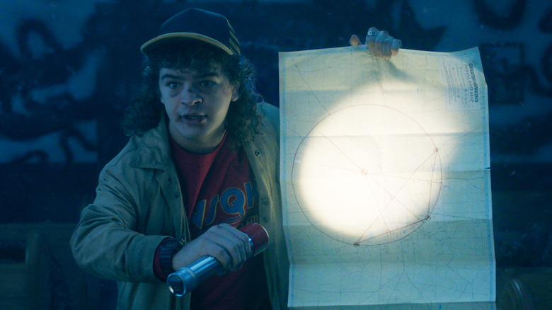Dustin (Gaten Matarazzo) shines a flashlight on a piece of paper in Stranger Things Season 5