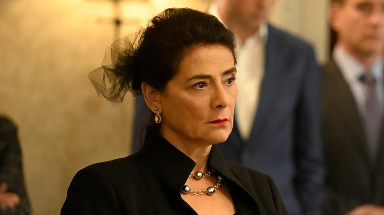 Hiam Abass as Marcia Roy, scowling in black attire at Logan's wake on Succession