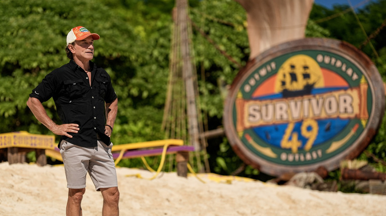 Jeff Probst stands in front of the Survivor 49 logo