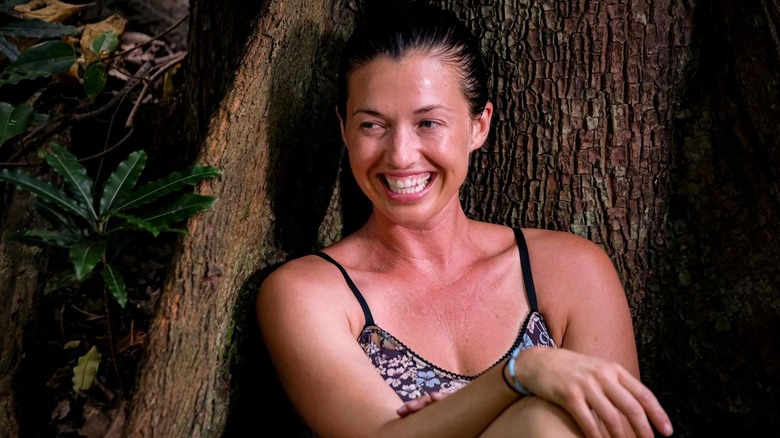 Parvati grinning and sitting against a tree on Survivor