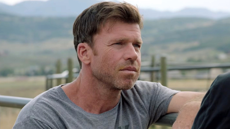 Taylor Sheridan leans against a fence outside on a ranch