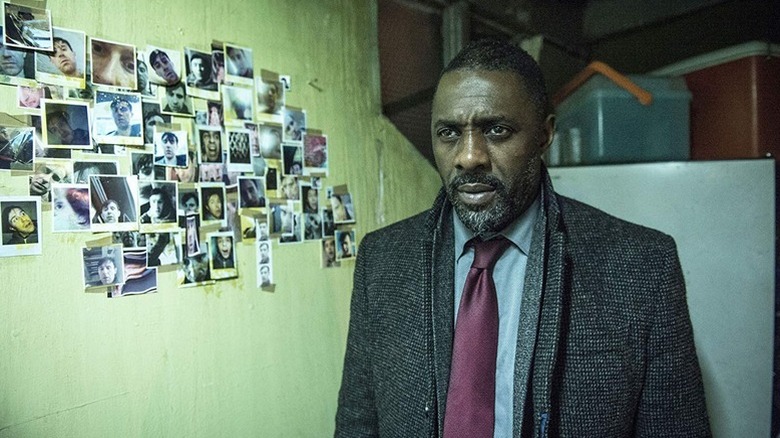 John Luther (Idris Elba) stands by a wall of pinned photographs on Luther