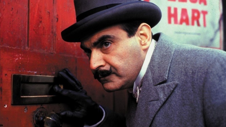 Hercule Poirot (David Suchet) examines a mail slot on a door on Poirot