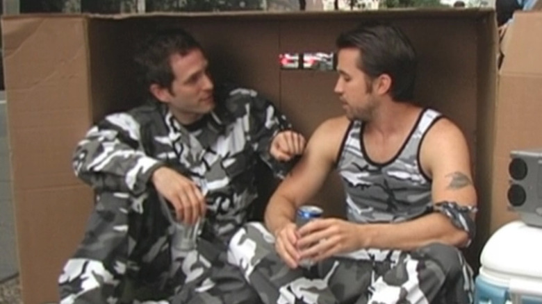 Glenn Howerton and Rob Mac as Dennis and Mac in grey camo drinking beers in a cardboard box on Always Sunny