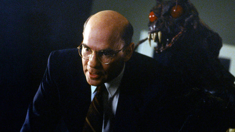 Mitch Pileggi as Walter Skinner leaning forward with giant beg with red eyes behind him in The X-Files