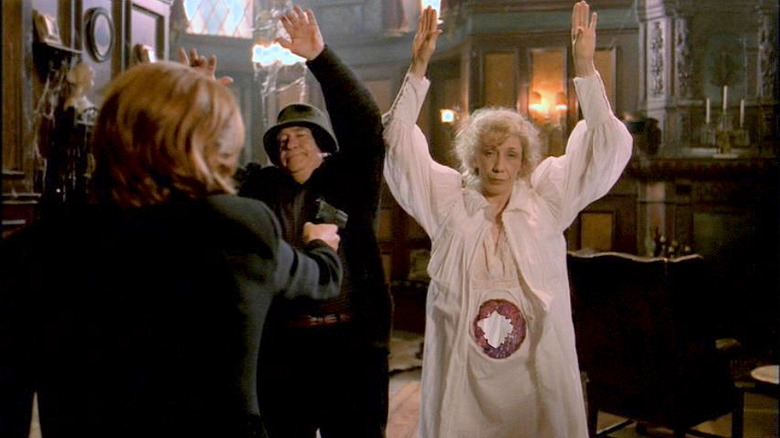 Gillian Anderson as Scully (face not visible) pointing gun at Ed Asner and Lily Tomlin with a hole in her stomach, both with their hands up, in The X-Files