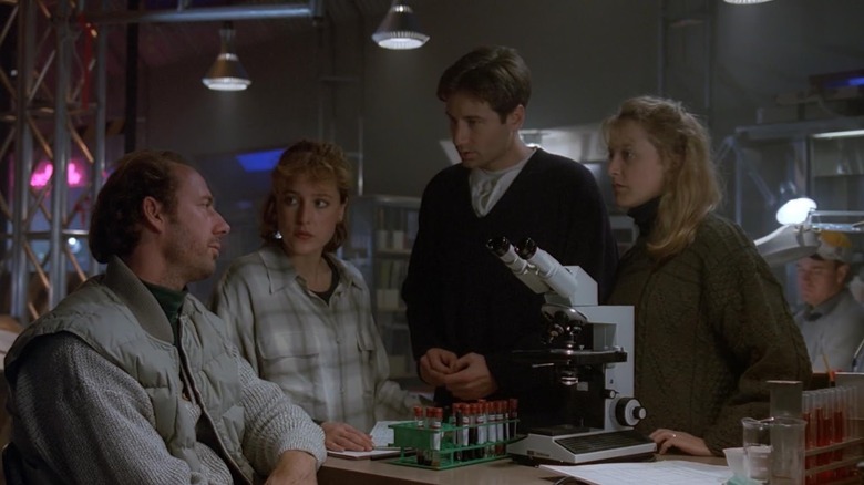 Xander Berkeley as Dr. Hodge sitting next to Gillian Anderson as Scully, David Duchovny as Mulder, and Felicity Huffman with vials and microscope in front of them in The X-Files