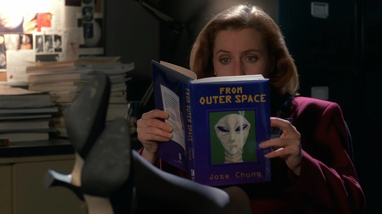 Gillian Anderson as Scully reading a purple book with alien on the cover called From Outer Space in The X-Files
