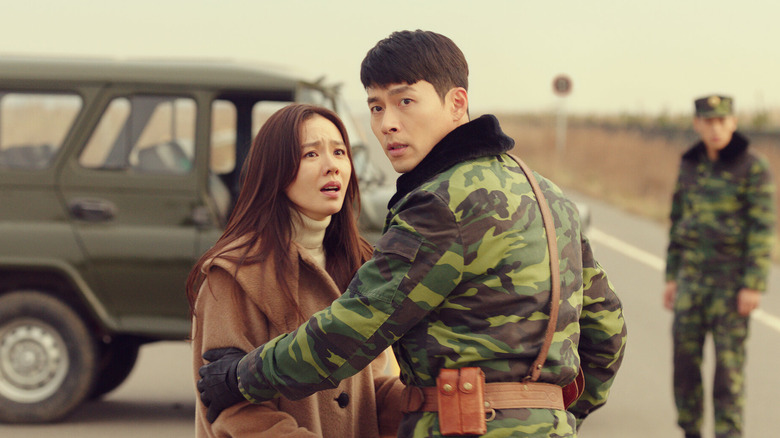 Ri Jeong-hyeok (Hyun Bin) escorts a distraught Yoon Se-ri (Son Ye-jin) towards a car on a road in Crash Landing on You
