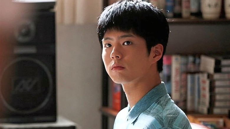 Choi Taek (Park Bo-gum) looks up inquisitively in a living room lit by sunlight on Reply 1988