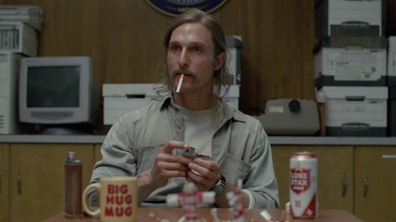 Matthew McConaughey with long hair smoking cigarette with Lone Star beer and mug in front of him as Rust Cohle on True Detective