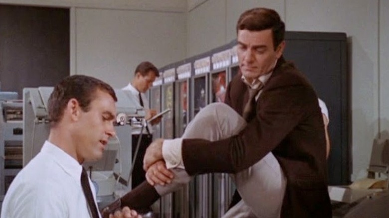 Joe Mannix (MIke Connors) sits on a desk surrounded by supercomputers in Mannix