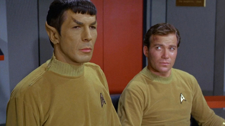 Captain Kirk (William Shatner) glances at Spock (Leonard Nimoy) standing beside him in Star Trek