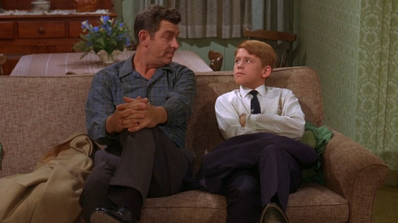 Andy Taylor (Andy Griffith) and Opie Taylor (Ron Howard) look at each other while sitting on a couch in The Andy Griffith Show