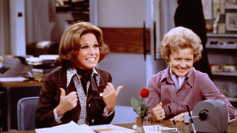 Mary Richards (Mary Tyler Moore) and Sue Ann Nivens (Betty White) laugh at a desk in The Mary Tyler Moore Show