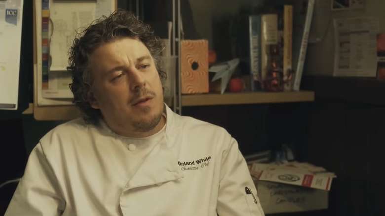 Alan Davies as Roland White, sitting in his office on Whites