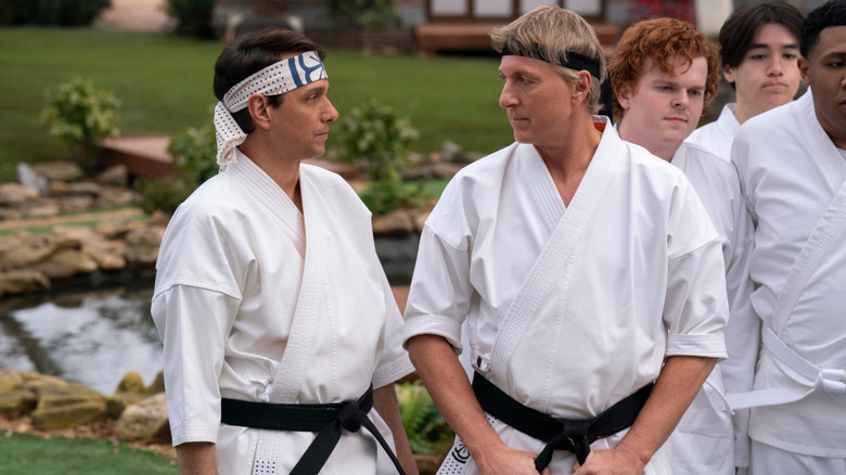 Daniel LaRusso (Ralph Macchio) and Johnny Lawrence (William Zabka) glance at each other next to their students while wearing karate gi on Cobra Kai